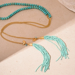 Vue détaillée des perles turquoise bohèmes et glands dorés sur un collier long chic