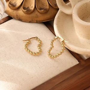 Detailed close-up of golden beaded hoop earrings on a beige linen fabric display