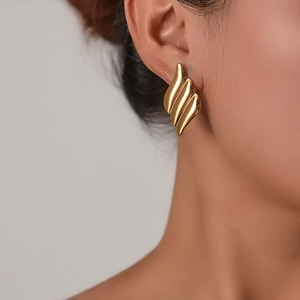 Detailed close-up showing gold wave-shaped earrings on a model to highlight metallic texture