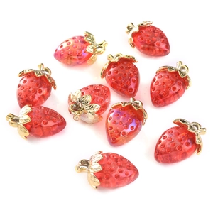 Close-up of red strawberry pendants with gold leaf caps on a plain white background