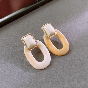 Detail of geometric resin earrings with gold woven frames and orange marble texture