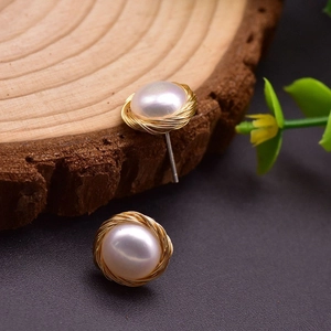 Macro shot of pearl earrings with intricate gold wire wrapping on a rustic wood slice