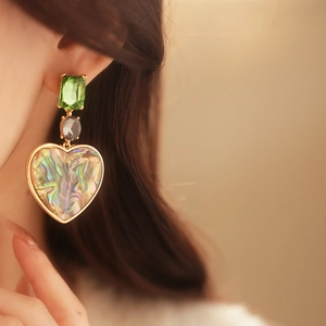 Close-up of vintage gold earrings with green gem, grey stone and iridescent shell heart