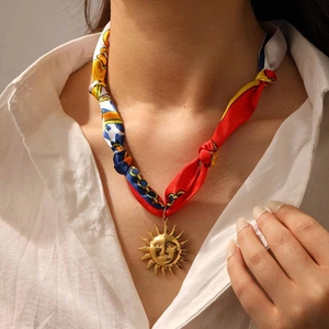 Gros plan sur un collier ruban aux motifs vibrants avec un grand pendentif soleil doré