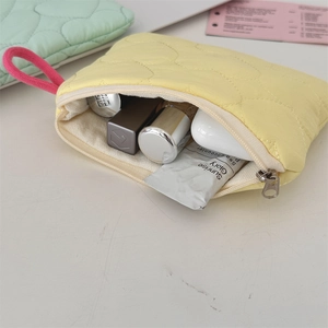 Flat lay of an open pale yellow quilted mini pouch showing cosmetics and pink zipper detail
