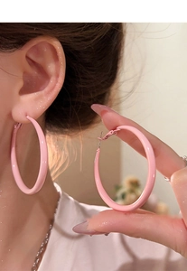 Close-up of oversized soft pink enamel hoop earrings with a glossy polished finish