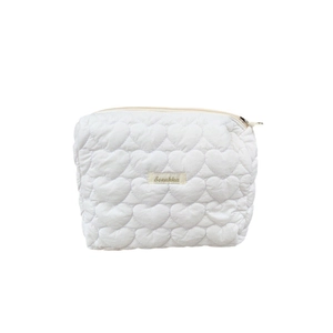 White quilted heart pattern makeup bag with zipper closure and logo tag on plain background