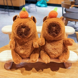 Pair of plush Capybara keychains with orange accessories sitting on a mini wooden bench