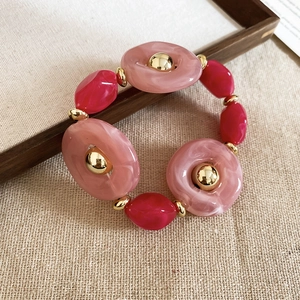 Detailed view of pink acrylic resin bracelet with golden beads on linen background