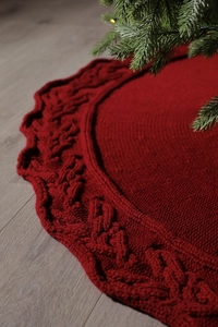 Close-up of red knit Christmas tree skirt with cable stitch pattern on wooden floor