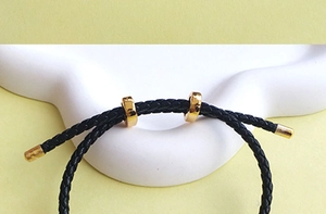 Close-up of black braided cord bracelet featuring adjustable gold sliding knots and end caps