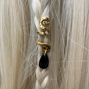 Detail of golden snake hair jewelry with black teardrop pendant on braided blonde hair