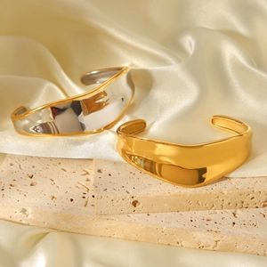 Detailed view of wave-shaped open bangles in gold and silver finish on stone