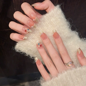 Detail of coffin-shaped press-on nails with golden glitter tips, pearls and colorful rhinestones