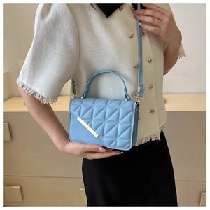Detail of light blue quilted square handbag featuring golden hardware and a removable strap