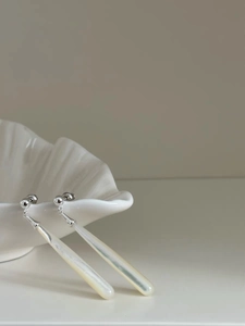 Detail view of silver teardrop earrings with white shell on a ceramic shell dish