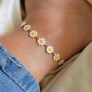 Detail view of a white daisy flower chain bracelet worn on wrist with denim background