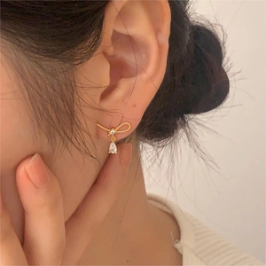 Detail of bow-shaped golden earring with a sparkling teardrop zircon on a model ear