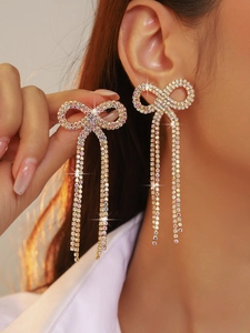 Detail of gold bow earrings with colorful rhinestones and long tassels on model