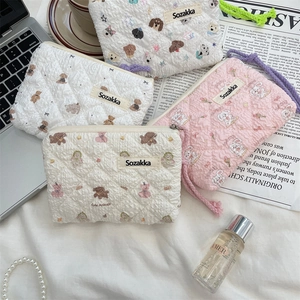 Flat lay of floral quilted pouches with cartoon animals, makeup and lifestyle props