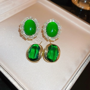 Macro shot of green oval and square gem earrings with gold frames in a jewelry box