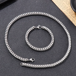 Macro shot of silver keeled link chain necklace and bracelet set on textured black background