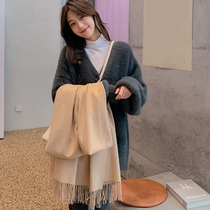 Detailed texture of beige cashmere scarf with tassels styled on a dark green cardigan