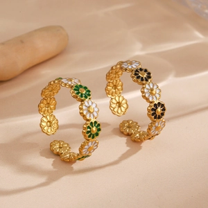Adjustable gold flower rings with colorful daisy enamel charms on a sandy surface