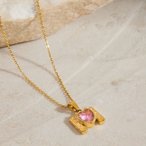 Detail of pink heart zircon pendant with hammered gold texture on a natural stone base