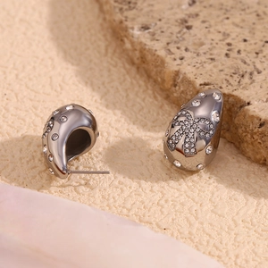 Detailed macro view of silver teardrop stud earrings with pavé crystals and bow accent