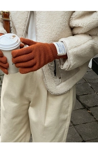Close-up of caramel wool knitted gloves with a vintage tag held by a model with coffee