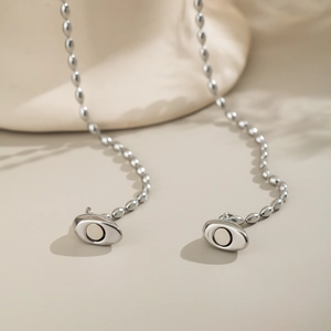 Détail de colliers à billes argentés avec pendentifs cœur magnétiques sur fond beige