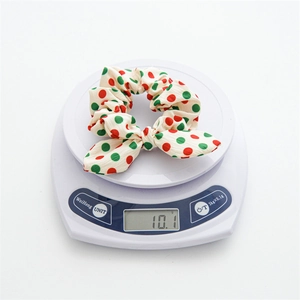 Christmas bow scrunchie with red and green polka dots on a white weighing scale