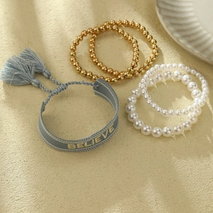 Detalle de 5 pulseras de playa con cuentas doradas, perlas y borla de tela azul