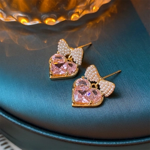 Detail of pink heart zircon earrings with pearl bow knot on dark teal silk surface