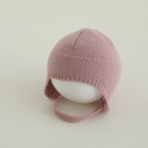 Dettaglio del cappello in maglia rosa per neonati con paraorecchie e trama a nido d'ape