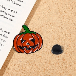 Cute Halloween pumpkin enamel pin badge with orange finish and green stem on cork background