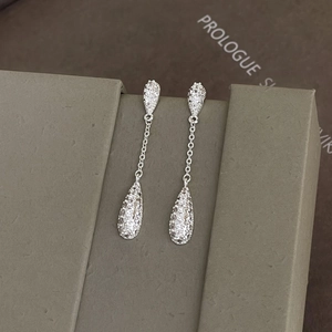 Macro shot of silver teardrop earrings with sparkling zircons on a textured jewelry box