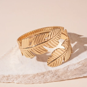 Macro view of a gold leaf-shaped metal cuff bracelet displayed on a natural stone base