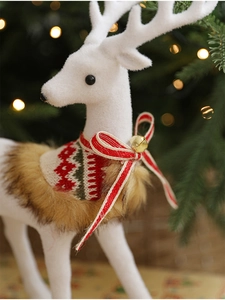 Close-up of white flocked reindeer with a knitted scarf and golden bell decoration