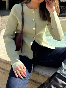 Detail of light green knit cardigan featuring elegant gold buttons and round neckline
