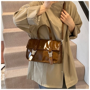 Brown patent leather satchel bag with silver buckles shown in a city lifestyle setting