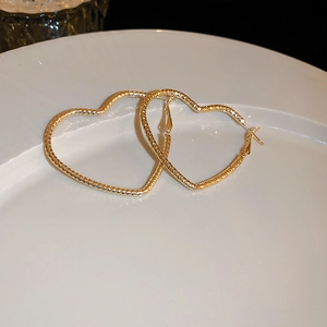 Detail of gold heart hoop earrings featuring a unique woven texture on a white plate