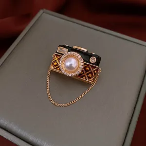 Vintage camera brooch with pearls, zircons, and black enamel on a luxury jewelry box