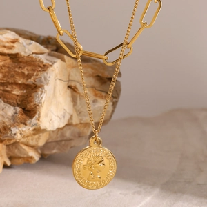 Macro detail of gold-plated multi-layer necklace with Elizabeth II coin pendant on rock