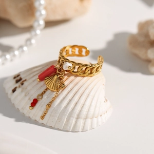 Macro detail of a gold seashell charm ring with red beads and white pearl fringe