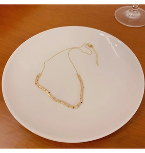 Close-up of gold beaded choker necklace featuring a lobster clasp on a white plate