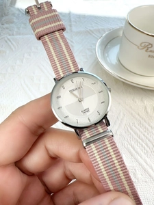 Detail view of a silver quartz watch with a striped fabric strap on lace background