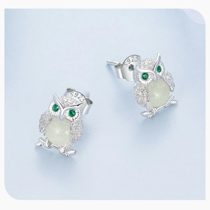 Macro detail of 925 sterling silver owl earrings with green gems and glowing beads