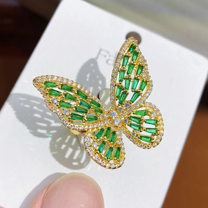 Close-up of golden butterfly ring with green gems and white crystals on a card